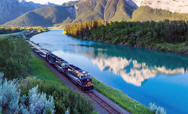 A train winding through a pine forest with mountains